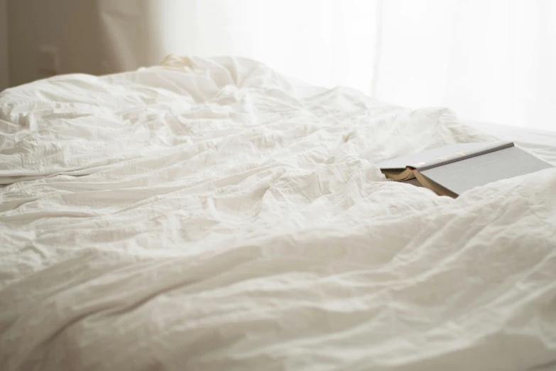 an unmade bed with a book on top of it, unsplash, happening, wearing white cloths, background image, angled view, white tablecloth