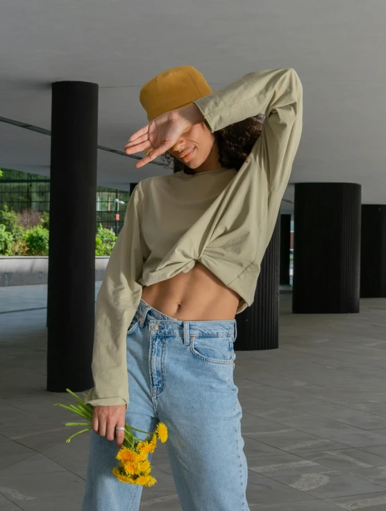 a woman standing on a skateboard holding a bunch of flowers, a colorized photo, by Nina Hamnett, trending on pexels, realism, wearing yellow croptop, sage green, long sleeve, wears a destroyed hat