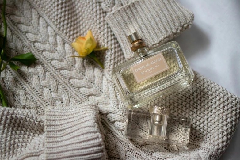 a bottle of perfume sitting on top of a sweater, inspired by Isobelle Ann Dods-Withers, light grey, lifestyle, ocher details, grey