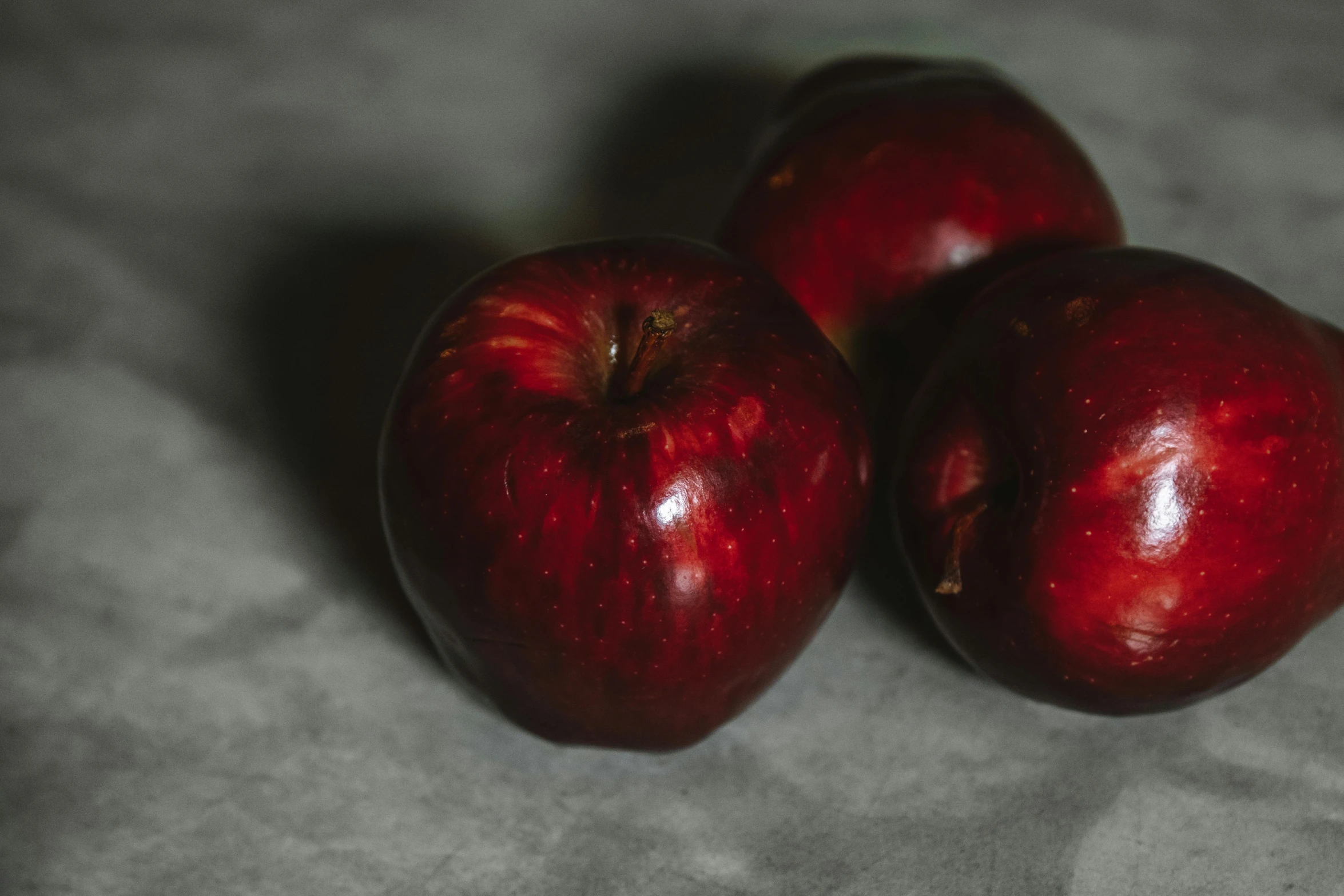 three red apples sitting on top of a table, by Emma Andijewska, pexels, on a gray background, background image, close - up photo, red velvet