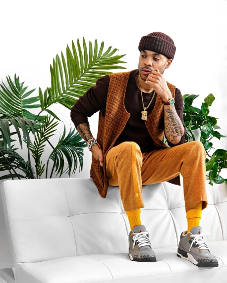 a man sitting on top of a white couch, an album cover, trending on pexels, baggy clothing and hat, ochre, model is wearing techtical vest, plants