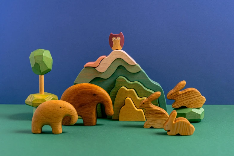 a group of wooden toys sitting on top of a table, inspired by Edward Lear, trending on unsplash, ecological art, standing in front of a mountain, fairytale animals, stylised, with radiating hill