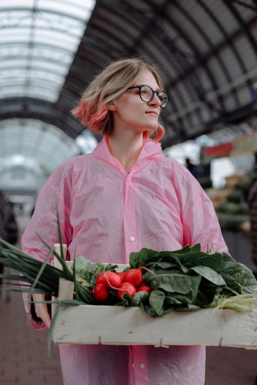 a woman in a pink raincoat holding a crate of vegetables, by Julia Pishtar, pexels contest winner, girl wearing round glasses, gif, market setting, androgynous person