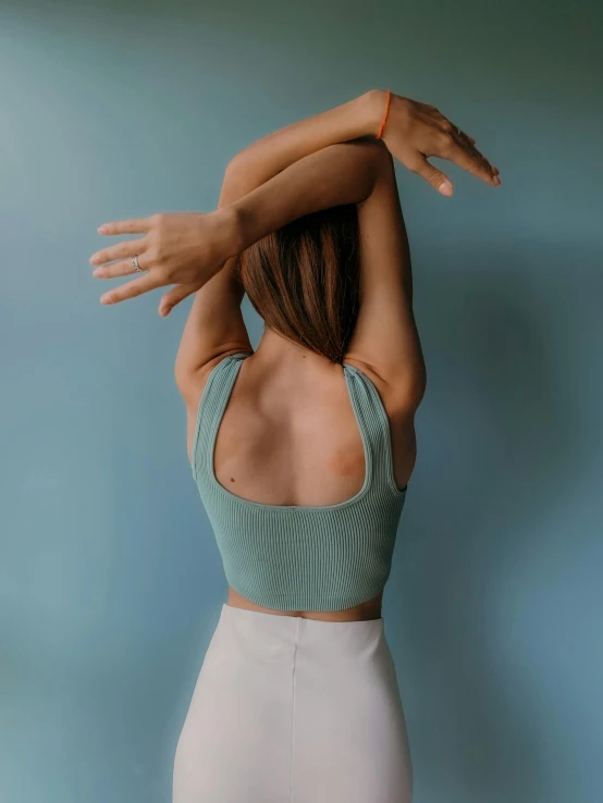 a woman standing in front of a blue wall, a colorized photo, trending on pexels, tight fitted tank top, back view », ((greenish blue tones)), arms stretched out