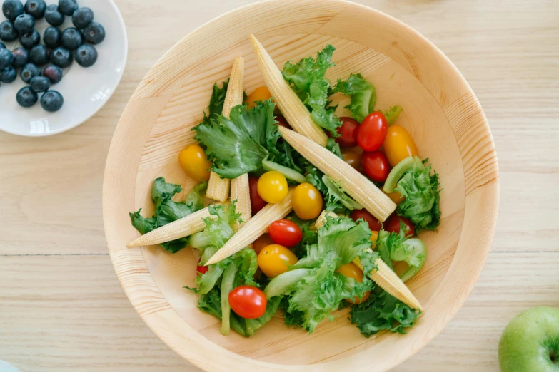 a wooden bowl filled with lettuce and tomatoes, by Nicolette Macnamara, eats bambus, yellow aureole, snacks, greens)