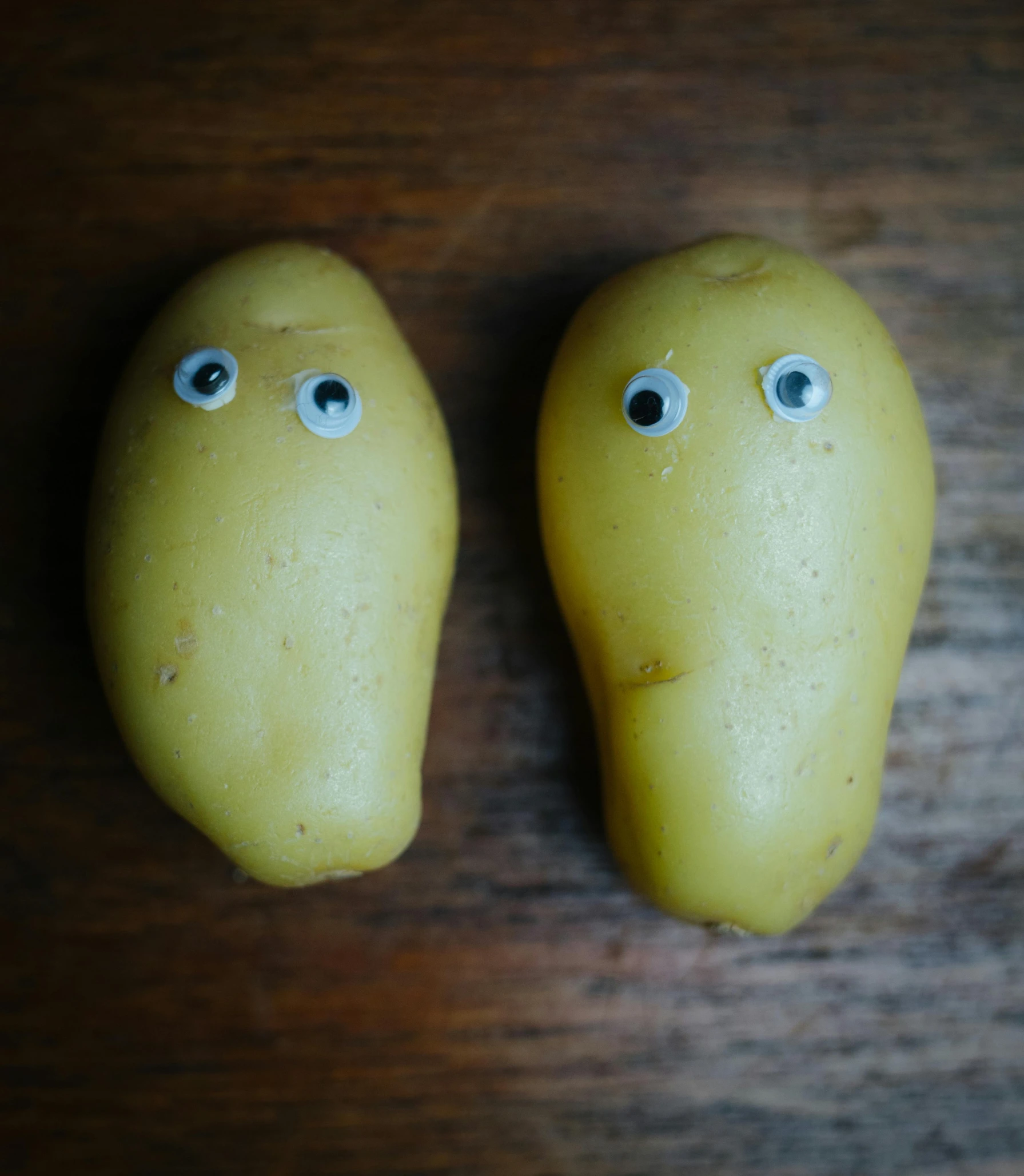 a couple of potatoes sitting on top of a wooden table, a cartoon, unsplash, purism, eyes are yellow, creepy macro photo, ignant, 🐿🍸🍋