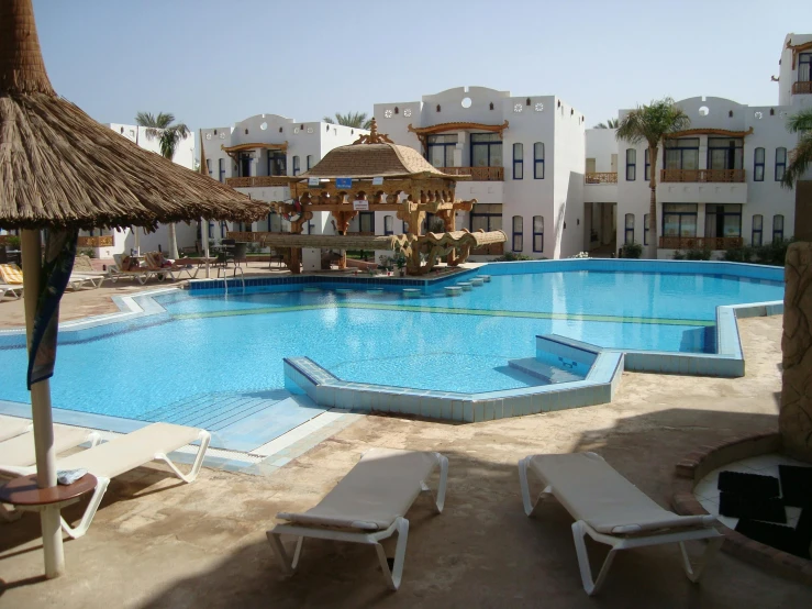 a group of lounge chairs sitting next to a swimming pool, in egypt, white houses, water park, well shaded