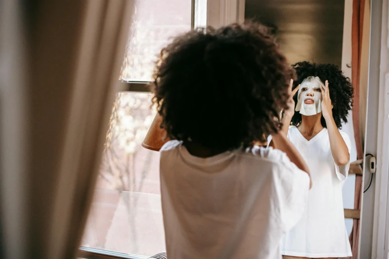 a woman brushing her hair in front of a mirror, pexels contest winner, wearing giant paper masks, light skinned african young girl, wearing a white hospital gown, morning time