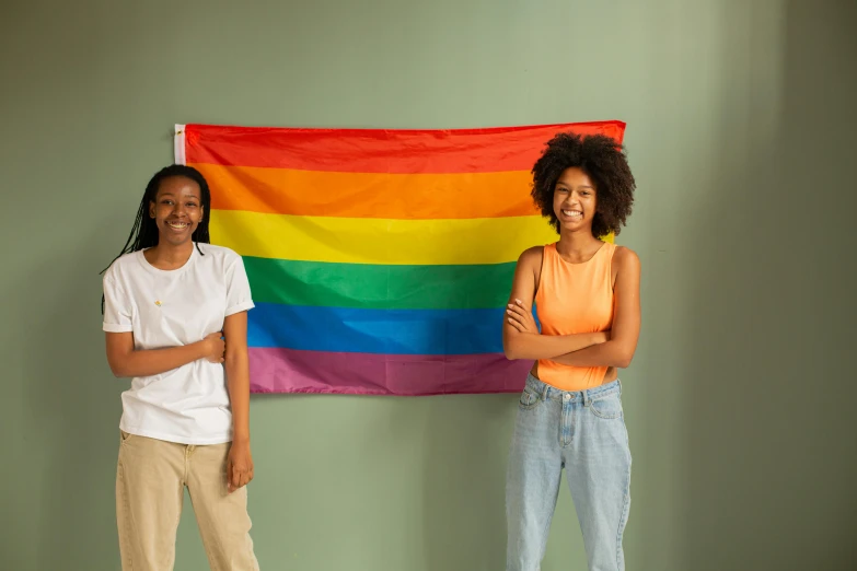 two women standing in front of a rainbow flag, trending on pexels, black teenage boy, standing in corner of room, banners, proud smile
