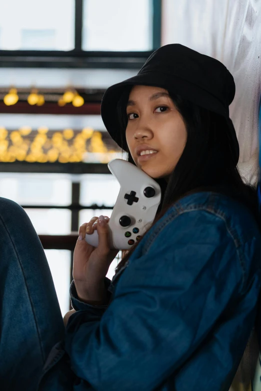 a woman sitting against a wall holding a video game controller, inspired by Zhu Da, unsplash, hat and hoodie, on ship, asian descent, xbox