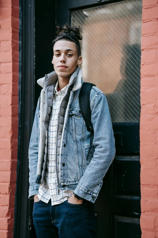 a man standing in front of a red brick building, jean jacket, non binary model, flannel, light skin tone