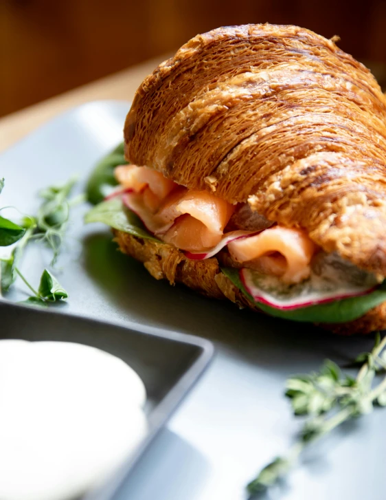 a croissant sandwich sitting on top of a blue plate, by Tom Bonson, unsplash, salmon khoshroo, a handsome, buxom, 0