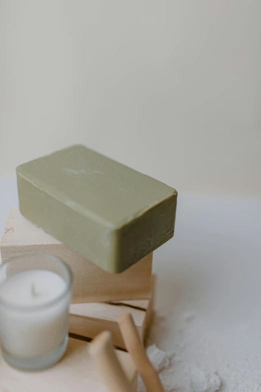 a soap bar sitting on top of a stack of books next to a candle, a marble sculpture, by Jessie Algie, unsplash, olive green, made of clay, mid body, #green