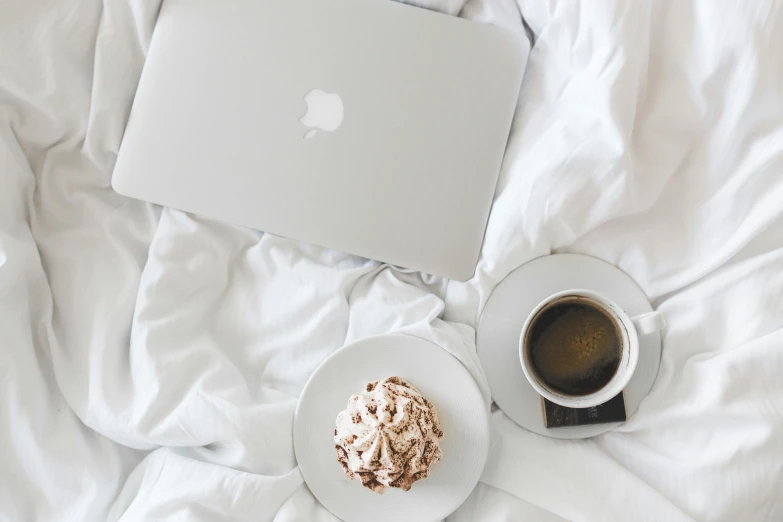 a laptop computer sitting on top of a bed next to a cup of coffee, by Carey Morris, trending on unsplash, whipped cream, with apple, white bed, background image