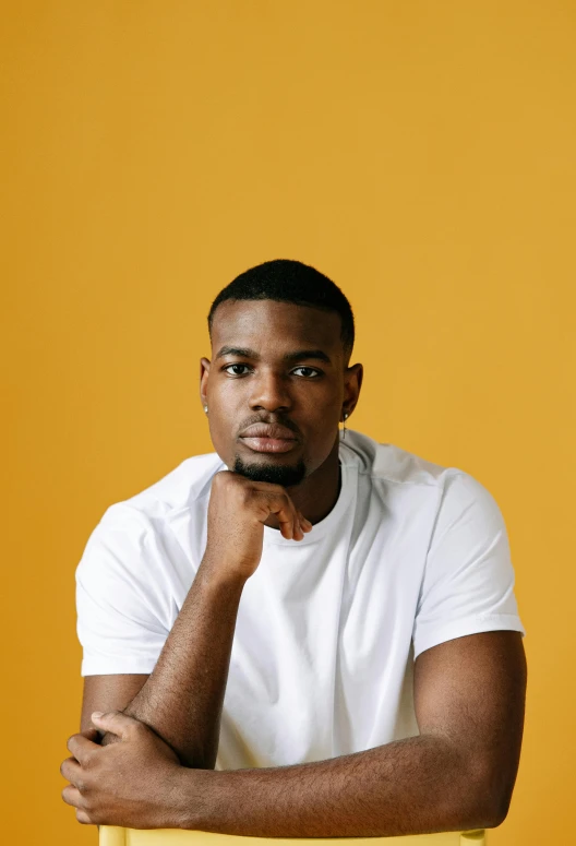 a man sitting on top of a yellow chair, inspired by Paul Georges, pexels contest winner, young man with beautiful face, maria borges, headshot profile picture, plain background