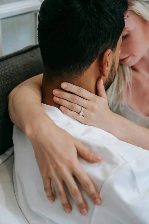 a man sitting next to a woman on top of a bed, trending on pexels, diamonds around her neck, embracing, detail shot, supportive