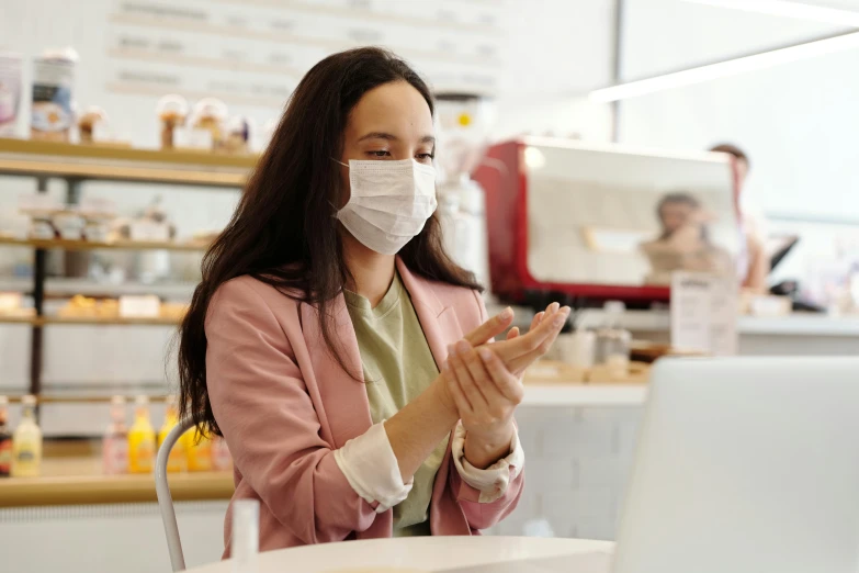 a woman sitting at a table in front of a laptop wearing a face mask, pexels, white bandages on fists, avatar image, pharmacy, a person standing in front of a