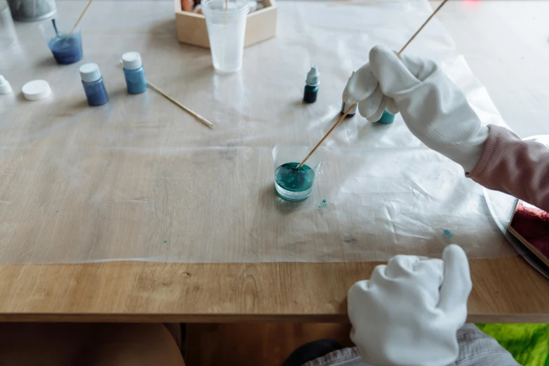 a person in white gloves painting on a wooden table, a hyperrealistic painting, inspired by Elsa Bleda, trending on unsplash, flowing teal-colored silk, candy treatments, water color nendoroid, lacquerware