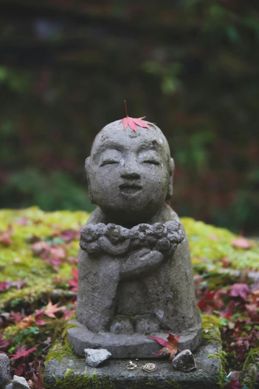 a statue sitting on top of a moss covered ground, inspired by Saneatsu Mushanokōji, unsplash, 🍁 cute, small details, serene smile, autum