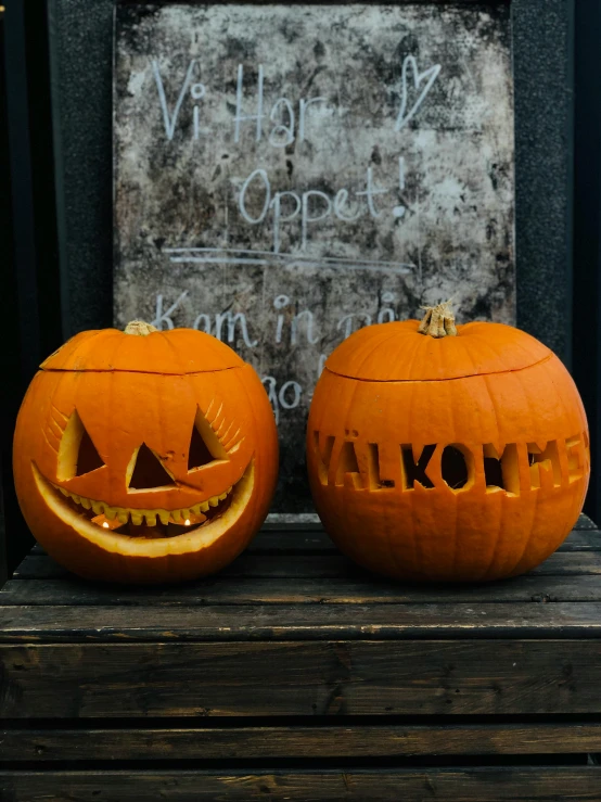 two carved pumpkins sitting on top of a wooden table, by Haukur Halldórsson, graffiti, promo image, welcoming, kanamemo, ready to eat