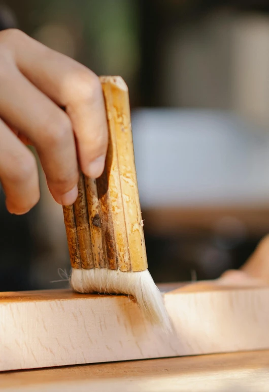 a person cutting a piece of wood with a knife, a detailed painting, inspired by Kanō Shōsenin, trending on unsplash, arts and crafts movement, large brush, brown, white, sake