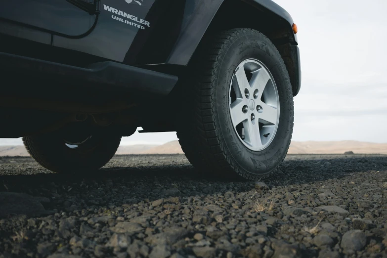 a black jeep parked on a gravel road, pexels contest winner, hyperrealism, detailed alloy wheels, profile close-up view, background image, graafland