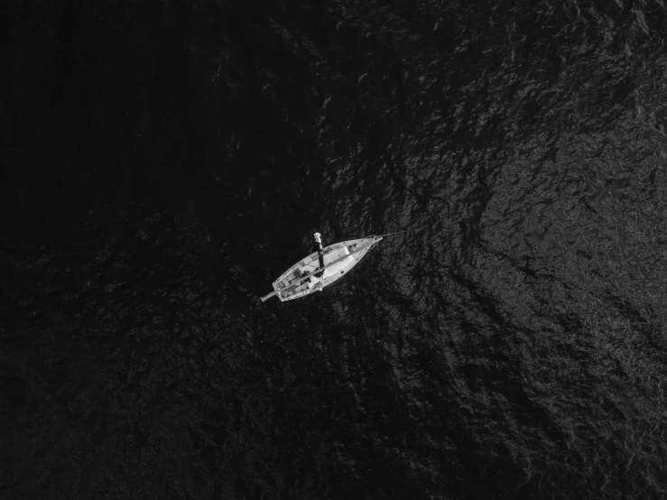 a small boat floating on top of a body of water, a black and white photo, by Adam Marczyński, pexels, drone footage, fisherman, dark backround, pose 4 of 1 6