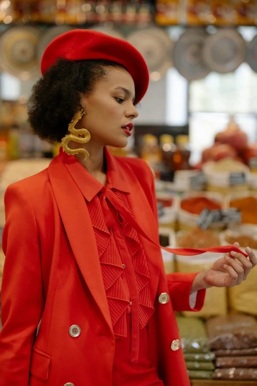 a woman in a red suit and hat in a store, by Adam Saks, trending on pexels, holding a snake, orange ribbons, vintage inspired, ashteroth