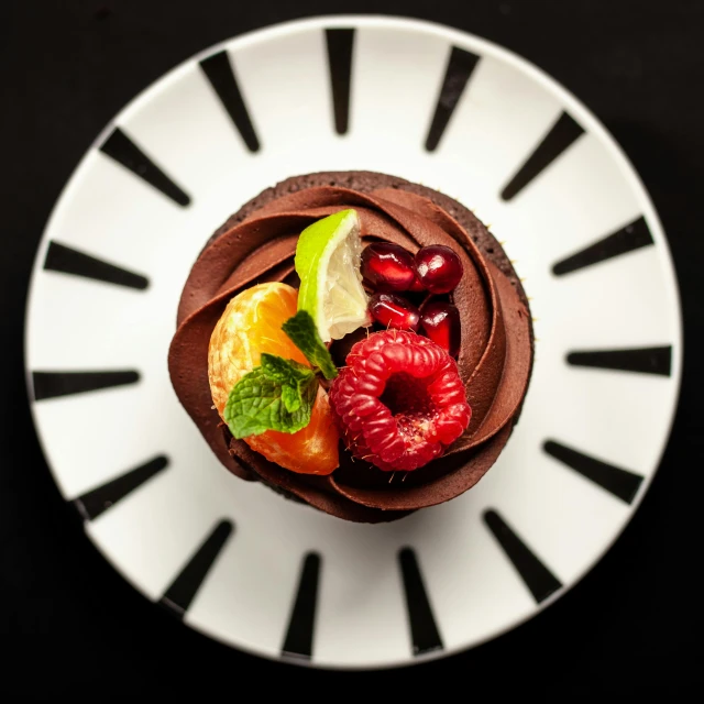 a chocolate cupcake sitting on top of a white plate, bowl of fruit, dark and intricate, bird's-eye view, high-quality photo