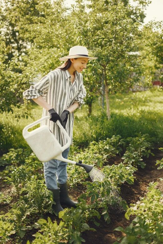 a woman that is standing in the grass with a watering can, wearing farm clothes, fruit trees, thumbnail, white