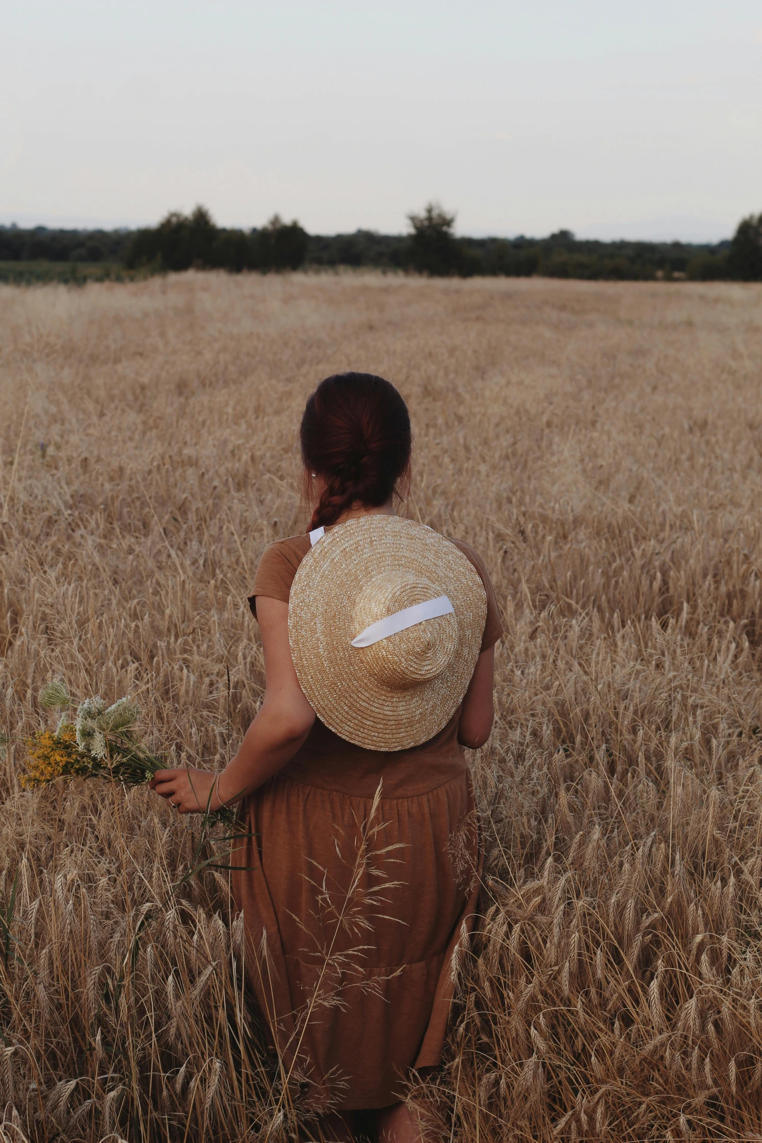 a woman standing in a field holding a bunch of flowers, pexels contest winner, renaissance, brown hat, facing away, low quality photo, straw