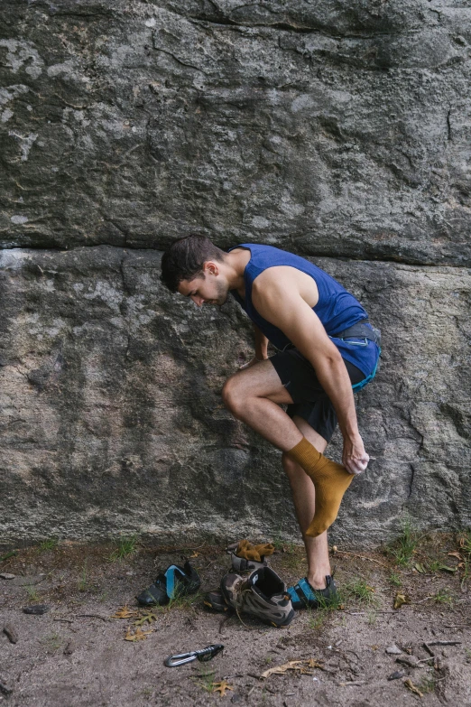 a man leaning against a rock next to a pair of shoes, by Jessie Algie, unsplash, renaissance, wearing leotard, belaying, wearing tank top, low quality photo