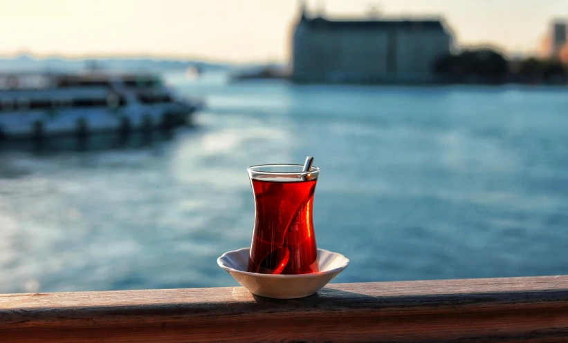 a cup of tea sitting on top of a white plate, by irakli nadar, pexels contest winner, hurufiyya, harbour, some red water, ottoman empire, drinking cocktail