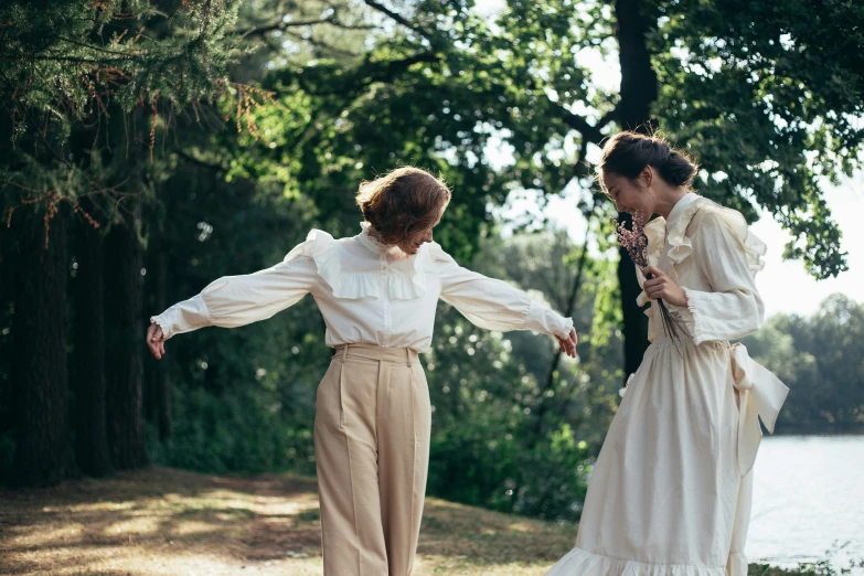 a couple of women standing next to each other, trending on pexels, renaissance, white clothes, vintage clothing, a park, dancing with each other