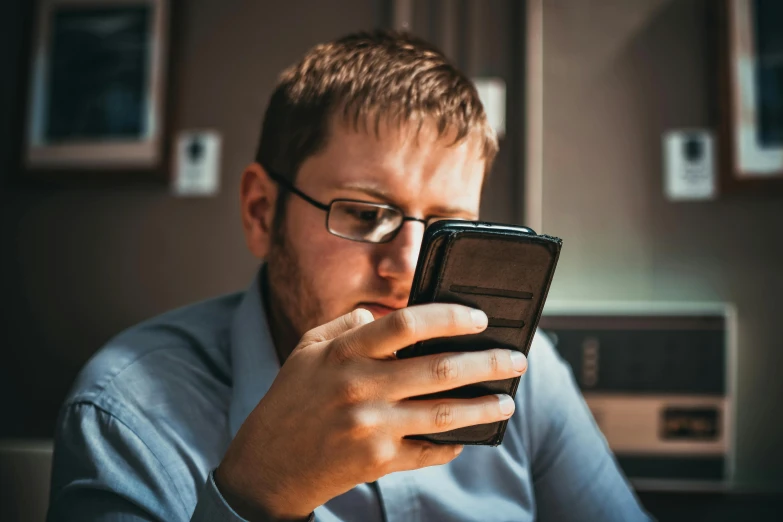 a man is looking at his cell phone, by Adam Marczyński, trending on pexels, square rimmed glasses, avatar image, caucasian, brown