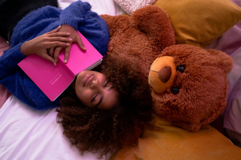 a woman laying on top of a bed next to a teddy bear, with book of science, dark brown skin, brown and magenta color scheme, bedhead