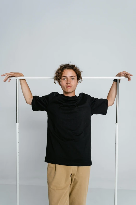 a man standing in front of a metal frame, wearing a black tshirt, white limbo, zac retz, curls on top