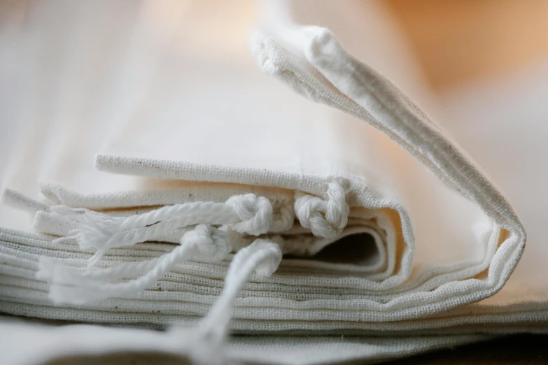 a stack of white towels sitting on top of a wooden table, by Helen Stevenson, unsplash, process art, pouches, ribbon, close up shot from the side, sustainable materials