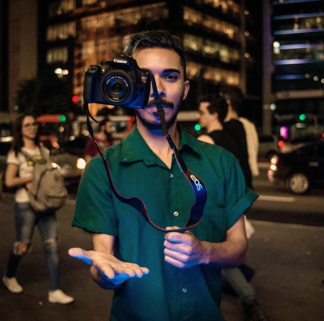 a man in a green shirt holding a camera, by Alejandro Obregón, pexels contest winner, photorealism, hero pose colorful city lighting, sneering at the camera, sony a 7 siii, sao paulo