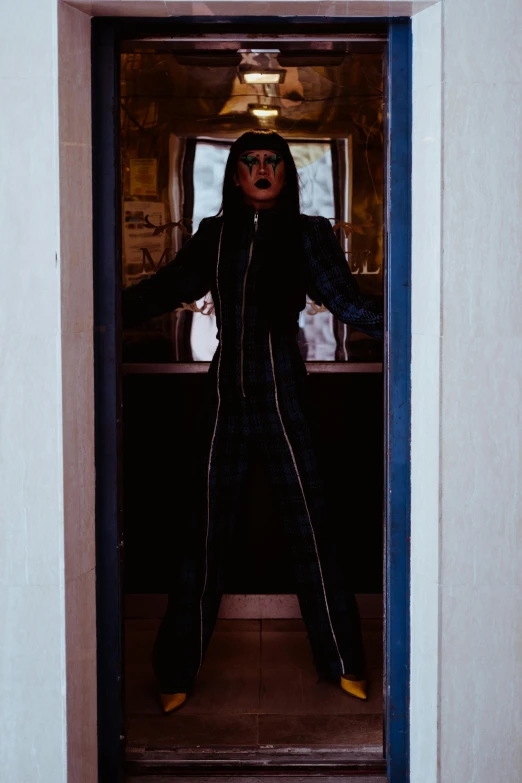 a man that is standing in a doorway, an album cover, by Winona Nelson, unsplash, bauhaus, goth cybersuit, drag, in suit with black glasses, full body devil woman