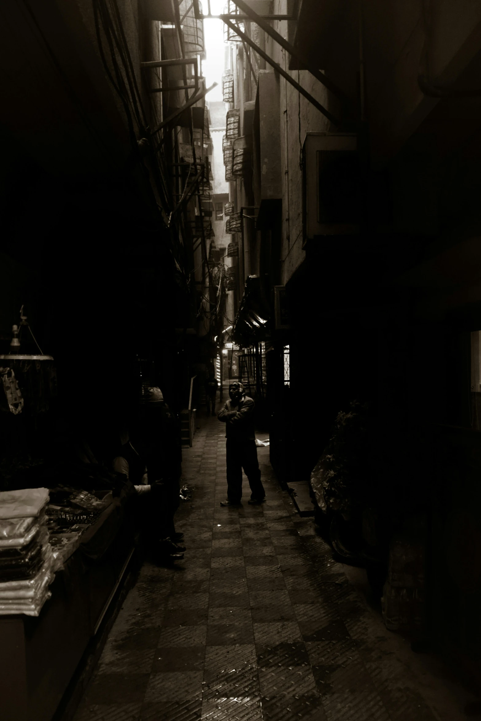 a black and white photo of people walking down a narrow alleyway, an album cover, by Modest Urgell, unsplash, dada, dark scene with dim light, taken in the late 2000s, vendors, mysterious man