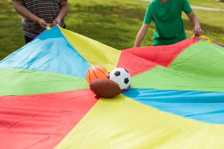 two young boys playing with a colorful parachute, dribble, game board, close up shot from the top, multicoloured, middle shot