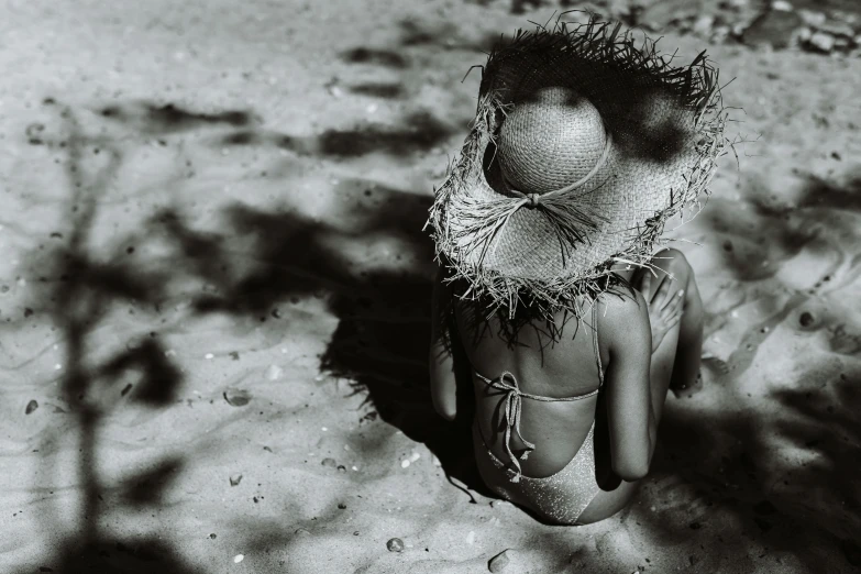 a black and white photo of a woman sitting in the sand, unsplash, surrealism, straw hat, faceless people, toy photography, dark-skinned