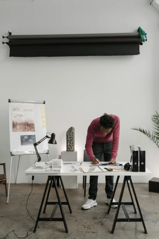 a person sitting at a table writing on a piece of paper, a picture, arbeitsrat für kunst, standing on a desk, archviz, dwell, curated collections