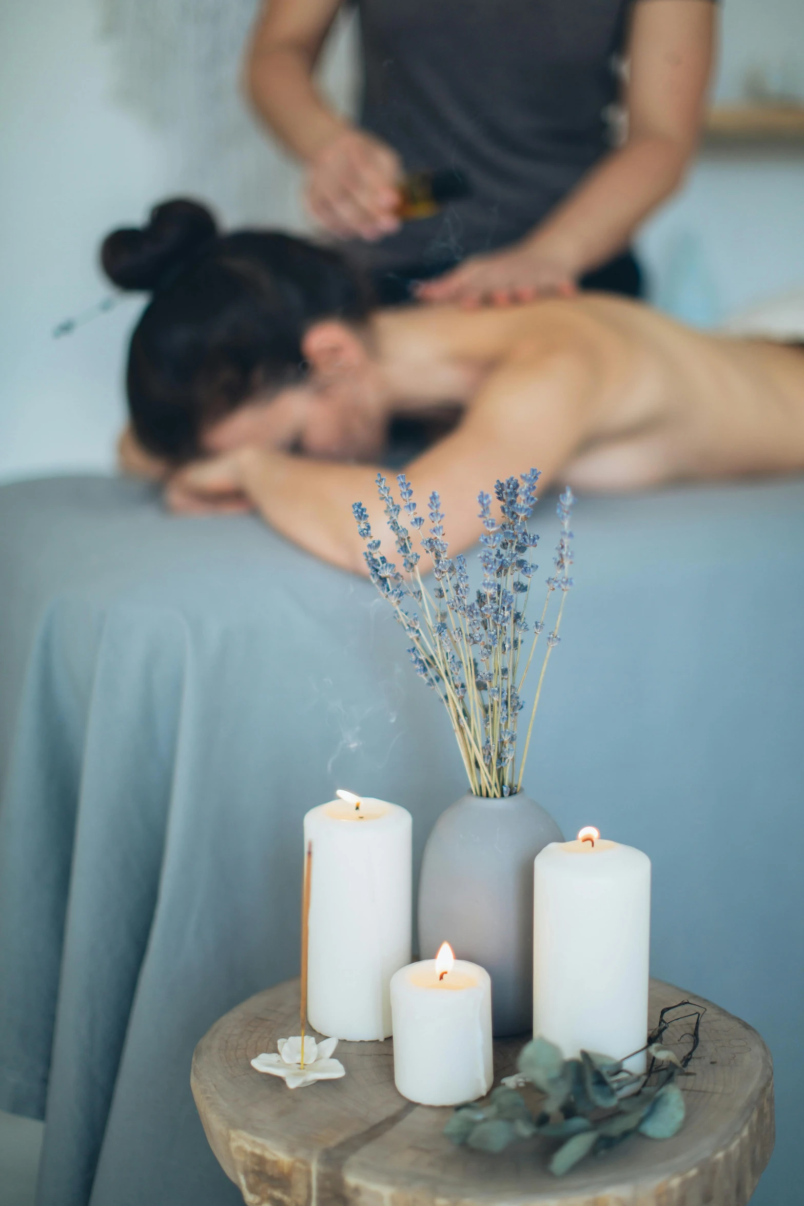 a woman getting a back massage at a spa, soft blue light, candles, lavender, grey