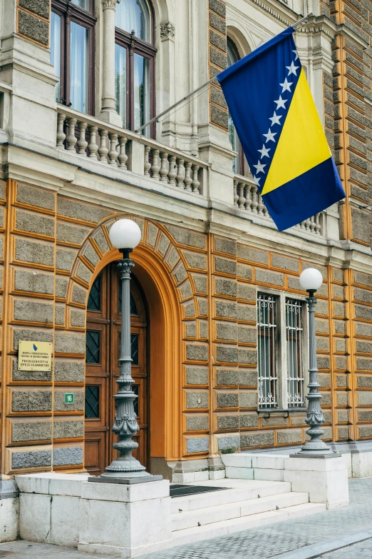 a building with a flag in front of it, inspired by Sava Šumanović, yellow, doorway, royal court, seven stars in right hand