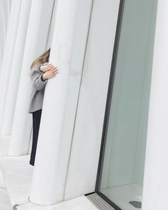 a woman that is standing in front of a building, a marble sculpture, inspired by David Chipperfield, trending on unsplash, brutalism, coat pleats, facepalm, colonnade, spying discretly