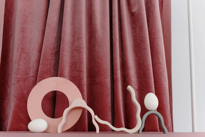 a couple of figurines sitting on top of a table, an abstract sculpture, inspired by Isamu Noguchi, trending on unsplash, plasticien, alizarin curtains, pink arches, round red m & m figure, velvet