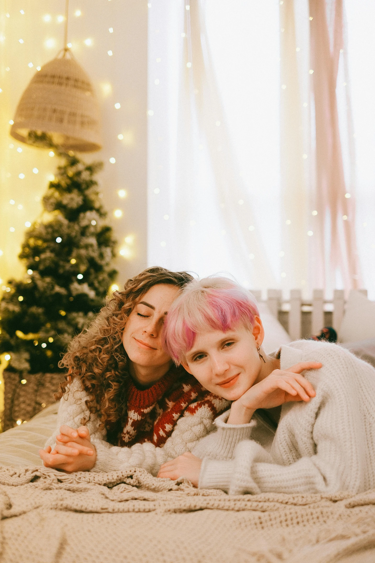 a couple of women laying on top of a bed, by Julia Pishtar, trending on pexels, wearing festive clothing, short pink hair, two buddies sitting in a room, hugging