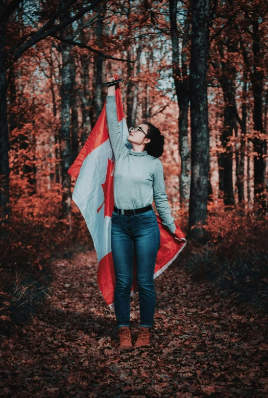 a woman holding a canadian flag in a forest, by Julia Pishtar, pexels contest winner, symbolism, triumphant pose, 🚿🗝📝, french girl, student